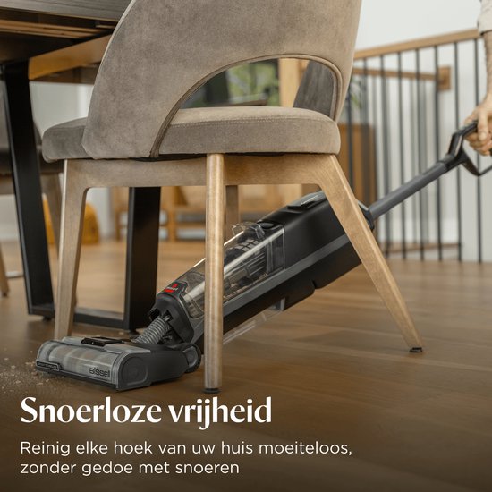 Zwarte BISSELL CrossWave stofzuiger met dweilfunctie, stofzuigt onder een stoel aan een tafel.