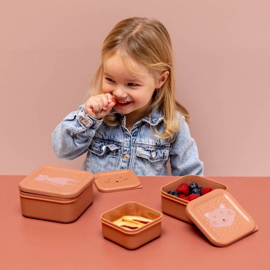 Meisje eet een snack; bruine Trixie snackdoosjes op tafel.