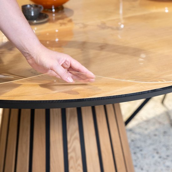Main posant un protège-table transparent sur une table ronde en bois.