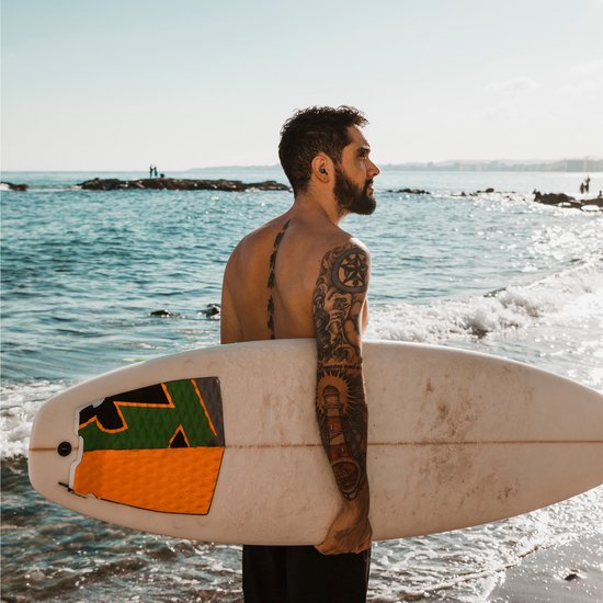 Man met surfplank op het strand, met zwarte oordopjes in.