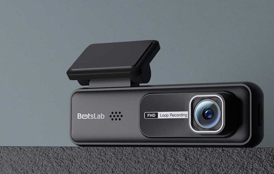 Zwarte dashcam met opzetstuk op een grijze ondergrond.