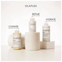 Drie Olaplex-producten staan op witte blokken. Verklarende pijlen wijzen naar 'CLEANSE', 'REPAIR' en 'HYDRATE'.