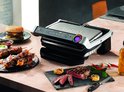 Tefal OptiGrill contactgrill op tafel, met steak, spiesjes en hamburger.
