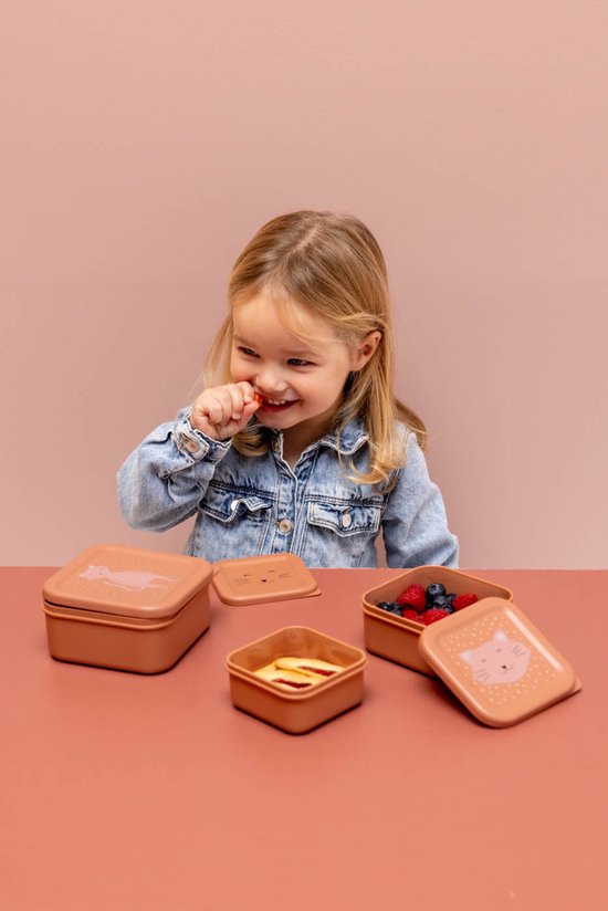 Kind met een spijkerjasje eet fruit uit vierkante, roestkleurige Mrs. Cat snackdoosjes.