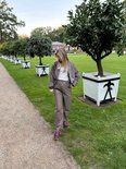Vrouw in een taupekleurige set van een bomberjack en broek met roze veterschoenen in een park.