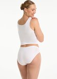 Model van achteren gezien, draagt een wit hemdje en een witte slip, lachend over haar schouder.