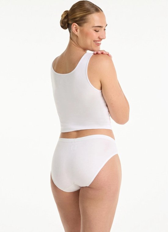 Model van achteren gezien, draagt een wit hemdje en een witte slip, lachend over haar schouder.