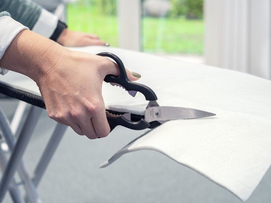 Close-up van een hand met schaar die de dikke, witte molton strijkplank onderlaag knipt.