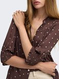 Model draagt bruine blouse met witte polkadotprint en gerimpelde mouwen tot 3/4.