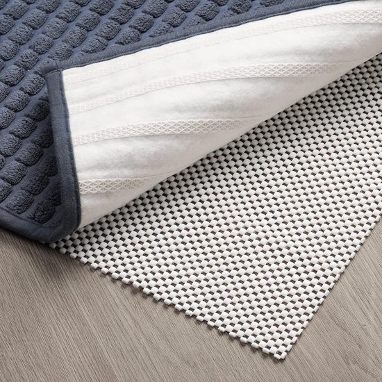 Onderkant van een donkergrijs vloerkleed met wit antislip onderkleed met rasterpatroon.
