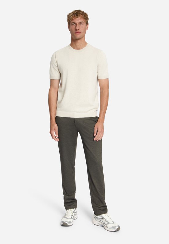 Man met een licht beige trui met korte mouwen en een donkerbruine jersey pantalon.