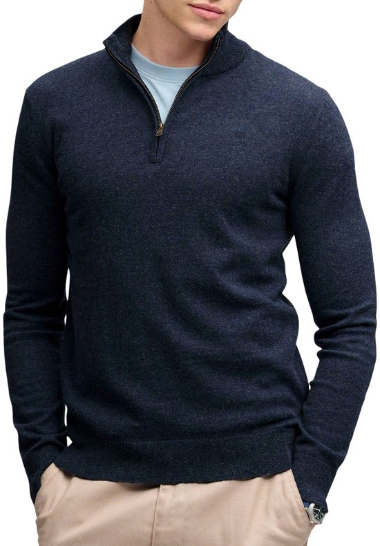 Man met donkerblauwe trui met rits, staande kraag en beige broek.