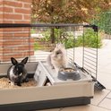 Twee konijnen, een zwarte met witte vlekken en een grijze, in een Krolik Extra Large kooi met voerbak.