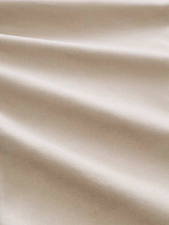 Close-up van de beige stof met subtiele textuur en plooien.