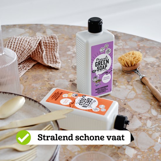 Twee flessen Marcel's Green Soap op een marmeren tafel. Eén fles sinaasappel & jasmijn, één fles lavendel & rozemarijn. Vaatwasborstel en servies.