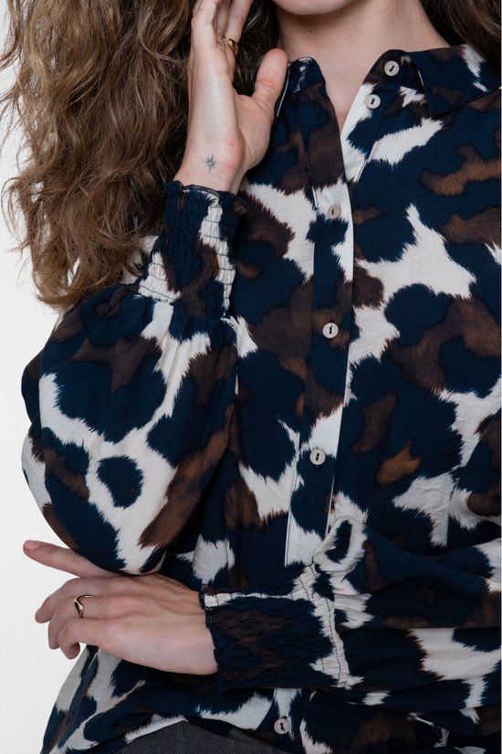 Close-up van een blouse met abstracte print in blauw, bruin en crème, met knoopsluiting en gesmokte mouwboorden.