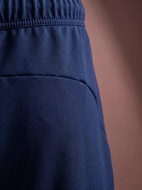Detail van de tailleband en zak van een marineblauwe joggingbroek.