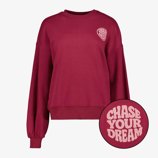Donkerrode trui met tekst 'CHASE YOUR DREAM' in roze cirkel op de borst.