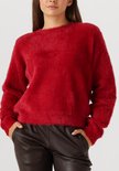 Een model draagt een rode, pluizige trui met lange mouwen en zwarte leren broek, met de handen in de zakken.