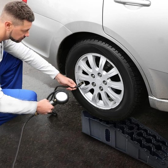 Man met bandenpomp controleert de bandenspanning van een auto op een oprijblok.