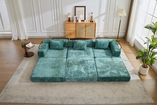 Uitgeklapte modulaire bank van donkergroene chenille, met kussens en ligvlak, op een vloerkleed.