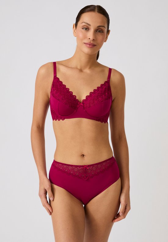 Model draagt een rode beugel-bh en bijpassende slip met kanten afwerking en strikdetail.