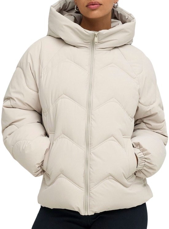 Model in een crèmekleurige pufferjas met kap en visgraatstiksels, handen in de zakken.