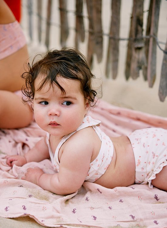 Baby met krullend donker haar draagt een crème bikini met vlinderprint en ruches.