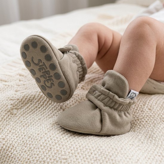 Close-up van babyvoeten in taupe slofjes met Steppies logo op de antislip-zolen.