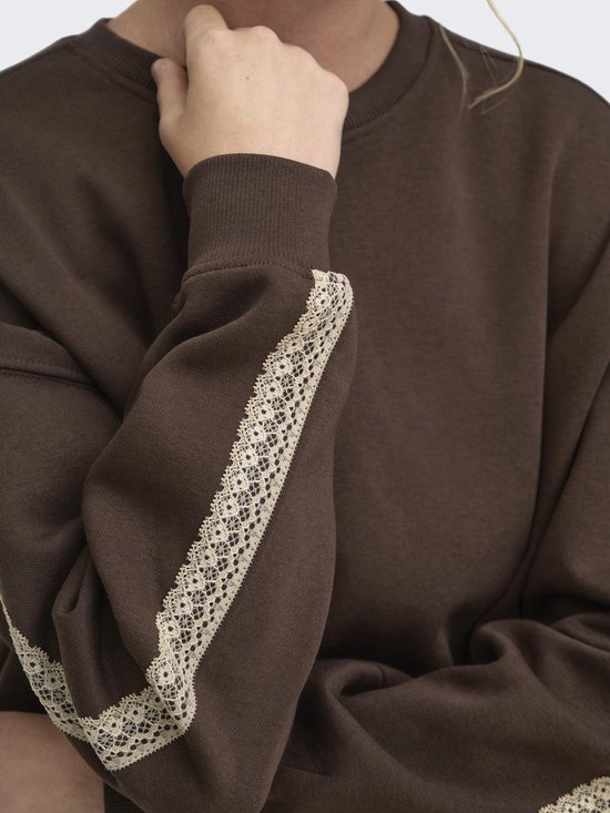 Close-up van de donkerbruine sweater met beige kanten bies langs de mouw.