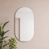 Ovale, frameloze Planetmöbel spiegel hangend aan een beige muur naast groene kamerplanten.