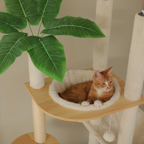 Oranje gestreepte kat met witte pootjes ligt in een zachte beige hangmat bij een plant.
