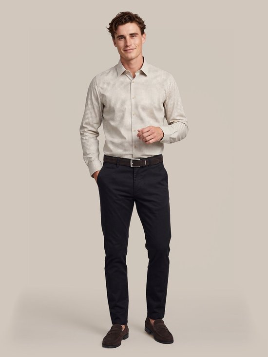 Model draagt een beige overhemd met een subtiel patroon, gecombineerd met een donkerblauwe broek en bruine loafers.
