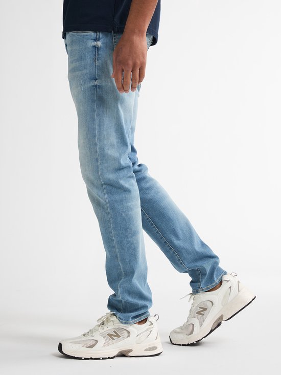 Blauwe slim fit jeans met vintage wassing, gedragen door een man met witte sneakers.