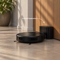 Zwarte robotstofzuiger keert terug naar het inbegrepen laadstation tegen een houten muur.