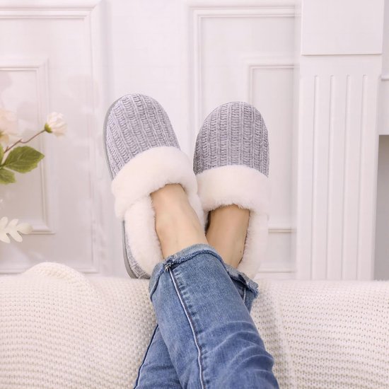 Voeten gekruist in grijze gebreide pantoffels met een witte pluche boord, gedragen met een jeans.