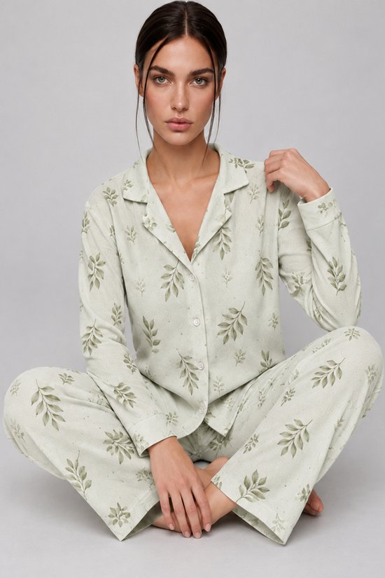 Model zit in kleermakerszit in een saliegroene pyjamaset met bladerenprint en lange mouwen.
