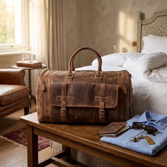 Luxe bruine leren weekendtas op een houten bankje, naast een overhemd, paspoort en zonnebril.