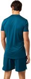 Man in petrolkleurig sportshirt en short, met zwarte tekst op de mouwen.