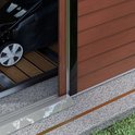 Detail van een schuifdeur van een bruin tuinhuis, met grasmaaier binnen.