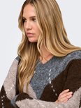 Close-up van model met lang blond haar, draagt een v-hals trui met argyle-patroon in grijs, bruin en beige.