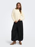 Model in een zachte crèmekleurige trui, gecombineerd met een zwarte wijde broek en bruine hakken.