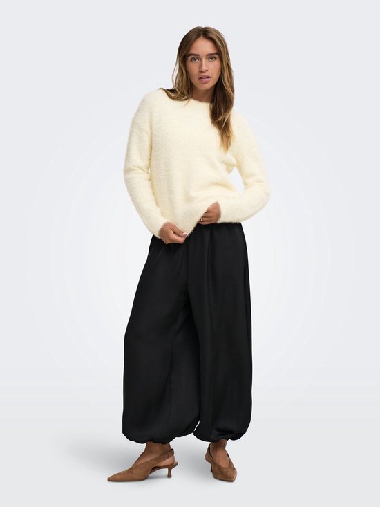 Model in een zachte crèmekleurige trui, gecombineerd met een zwarte wijde broek en bruine hakken.