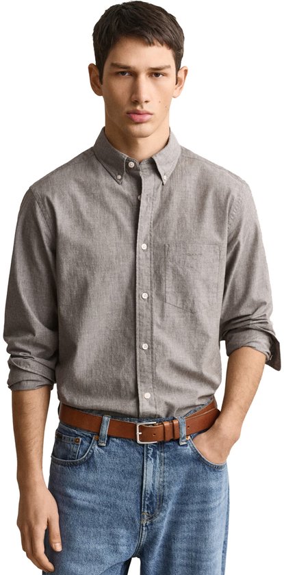 Model draagt een grijs Gant-overhemd met knoopjes, borstzak en bruine riem bij een blauwe jeans.