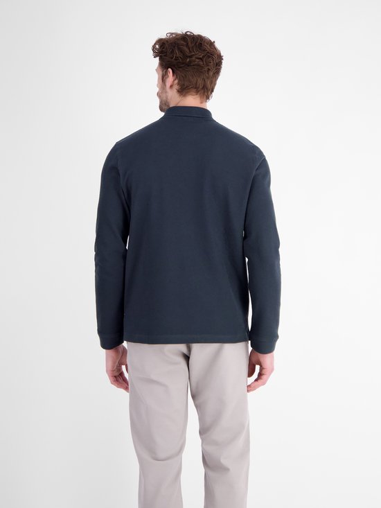 Achteraanzicht van een model in een marineblauw poloshirt met lange mouwen en grijsbeige broek.