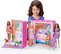 Een kind speelt met Barbiepoppen en een openklapbaar vakantiehuis met keuken en garage.