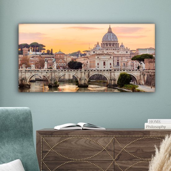 Canvas van de Sint-Pietersbasiliek en de Ponte Sant'Angelo in Rome bij zonsondergang, hangend boven een donker dressoir.