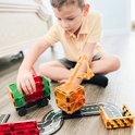 Jongetje speelt met Magna-Tiles. Hij bouwt met transparante blokken, inclusief een hijskraan en een vrachtwagen met groene en rode lading.