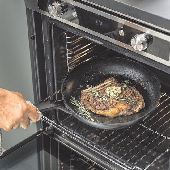 Man haalt koekenpan met biefstuk en rozemarijn uit een oven.