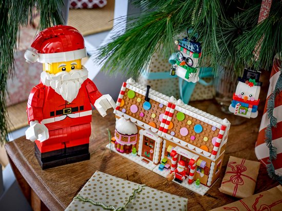 LEGO opgeschaalde Kerstman minifiguur naast een LEGO peperkoekhuisje onder een kerstboom.